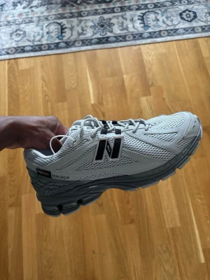 New Balance 1906R Gore-Tex sneakers - Snygga New Balance 1906R sneakers i ljusgrå mesh och syntet med Gore-Tex-detaljer. Skorna har en chunky sula i grått och svart, samt stora N-loggor på sidorna. Perfekta för dig som gillar sportig och modern stil.