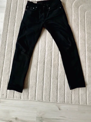 Svarta Levi's jeans raka ben - Säljer ett par svarta jeans från Levi's med klassisk femficksmodell och raka ben. Jeansen har Levi's ikoniska bakfickor med söm och röd etikett. Materialet är slitstarkt denim i bomull. Perfekta för en clean och stilren look. modell 502