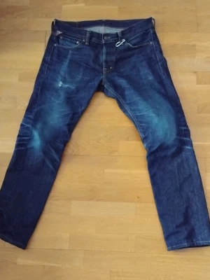 Ralph Lauren jeans - Säljer ett par mörkblå jeans från Denim & Supply Ralph Lauren. Klassisk femficksmodell med snygga kontrastsömmar och en liten detalj med amerikansk flagga vid fickan. Jeansen har rak passform och är tillverkade i slitstarkt bomullsdenim.