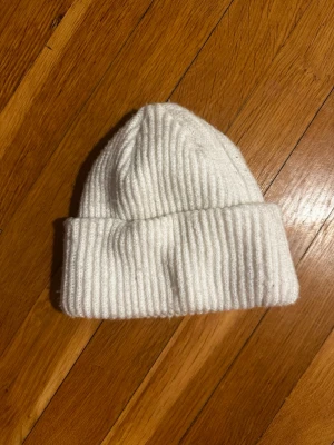 Vit ribbstickad mössa - Säljer en stilren vit ribbstickad mössa med uppvikt kant. Perfekt för kalla dagar och enkel att matcha med olika outfits. Mössan har en klassisk form och är tillverkad i mjukt material som håller dig varm. Lite nopprig 