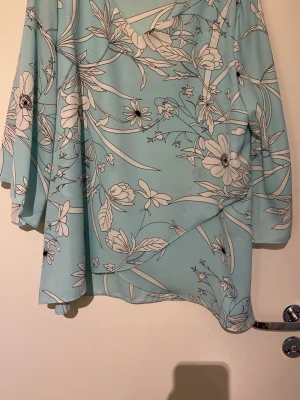 Blommig ljusblå blus från Isolde - Ljusblå blus från Isolde med vita och svarta blommönster. Blusen har v-ringning och vida, trekvartsärmar. Tillverkad i ett tunt, flowy material som ger en luftig känsla. Perfekt för dig som gillar en avslappnad men ändå stilren look.