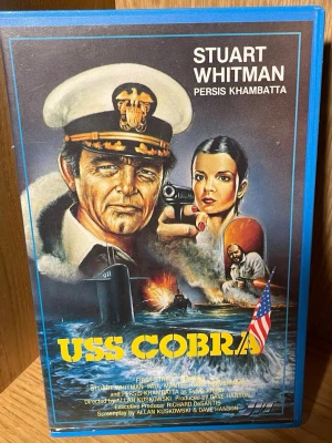 USS Cobra VHS - Spännande VHS med militärtema där USA och Sovjet byter fångar ombord på en ubåt. Omslaget har dramatiska illustrationer med ubåt, explosioner och amerikansk flagga. Perfekt för dig som gillar action, kalla kriget och äventyr.