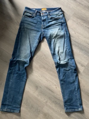 Blå jeans med raka ben - Säljer ett par blå snygga blå jeans från Jack & Jones med skön fade på framsidan. Modellen på jeansen är Tapered/mike. Jeansen har normal midja, dragkedjegylf och är tillverkade i denim med stretch för extra komfort. Perfekta för en avslappnad och trendig look. 