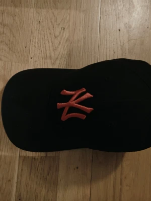 Svart New York Yankees keps - Snygg svart keps från New Era med klassisk New York Yankees-logga broderad i rött framtill. Kepsen har böjd skärm och justerbar rem baktill för perfekt passform. Tillverkad i bomull för en bekväm känsla.