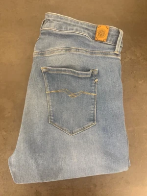 Ljusblå Replay Luizen jeans stl 32/30 - Snygga ljusblå slim jeans från Replay med klassisk femficksmodell och diskreta slitningar framtill. Jeansen har en hög midja och är tillverkade i stretchigt denim för en bekväm passform. Perfekta till sneakers eller boots.