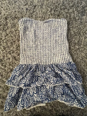 Vit och blå axelbandslös volangklänning - Säker en klänning från Gina i storlek 170. Sitter som e XS/S. Använd två gånger. Skriv om du undrar nått💕