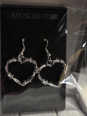 Hjärnformade örhängen i rostfritt stål - Säljer ett par coola örhängen i form av hjärtan, designade som taggtråd. De är silvriga och gjorda i rostfritt stål, vilket ger en edgy och unik look. Perfekta för dig som vill sticka ut med dina accessoarer.
