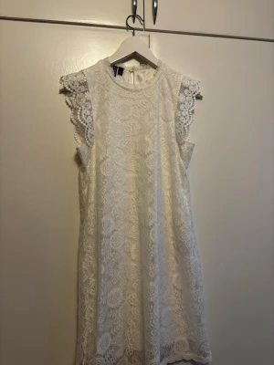 Vit spetsklänning med korta ärmar - Säljer en vit kort klänning från Pieces  i vacker spets med detaljerade mönster. Klänningen har ärmlös design med spetsvolang vid axlarna och rund halsringning. Perfekt för sommarens alla tillfällen och studentfirande. Pris kan diskuteras😊