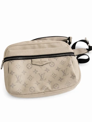 Vit axelväska från Louis Vuitton - Snygg vit axelväska från Louis Vuitton med klassiskt monogrammönster i grått. Väskan har en rektangulär form, svart justerbar axelrem och en praktisk ytterficka med dragkedja. Tillverkad i tåligt canvasmaterial som ger en exklusiv känsla.