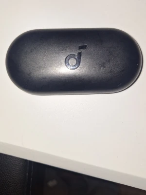 Svarta in-ear hörlurar från Anker - Trådlösa in-ear hörlurar från Anker med svart, oval laddningsetui och diskret logotyp på locket. Hörlurarna har en modern design och är tillverkade i plast. Perfekt för musik och samtal på språng.