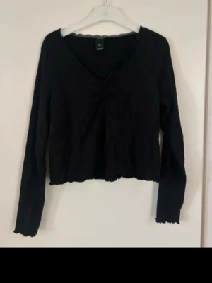 Svart croppad långärmad topp från H&M - Svart långärmad topp från H&M med v-ringad hals och croppad passform. Tillverkad i mjuk bomull och har subtila spetsdetaljer längs halsen. Perfekt för dig som gillar en enkel och stilren look.