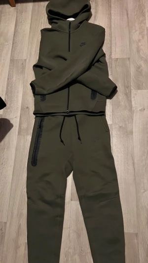 Olivgrön Nike tech tracksuit med huva - Säljer denna nike tech tracksuit från nike, använd några fåtal gånger men finns inga problem på den.
