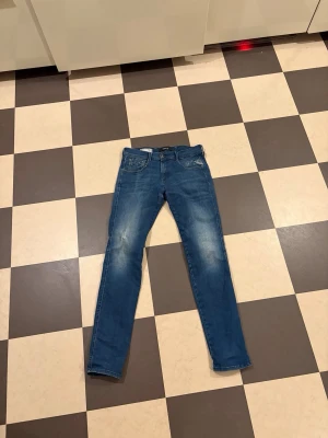Blåa Replay model anbass - Säljer ett par blåjeans från Replay med klassisk femficksmodell och snygga slitningar framtill. Jeansen har normal midja, dragkedjegylf och är tillverkade i mjukt denimtyg som ger en skön passform. Perfekta för dig som gillar en avslappnad men trendig stil. W29 L32
