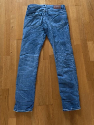 Blå raka jeans från Boss - Blå jeans från Boss i klassisk femficksmodell med raka ben och normal passform. Jeansen är tillverkade i mjuk bomullsdenim och har en ljus tvätt som ger en avslappnad vibe. Perfekta för dig som gillar stilrena och tidlösa jeans.