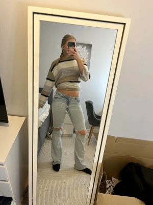 Randig stickad tröja  - Trendig stickad tröja med breda ränder i beige, grått, vitt och svart. Modellen är croppad med avslappnad passform och långa ärmar. Mjuk och skön, perfekt för en chill look.