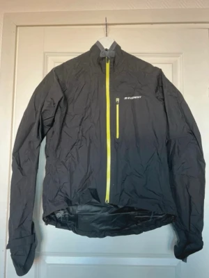 Svart Everest Regnjacka / Träningsjacka - Enkel och klassisk svart Everest vind och regn-jacka med neongröna detaljer. Bra använt skick. Skydd över händerna med en resår för fingret. Dragsko i botten på jackan. Reflex och ficka baktill. Ficka innanför jackan som har öppnats upp, går säkert att stänga ihop igen (bild 3). Storlek 36, normal i storleken.