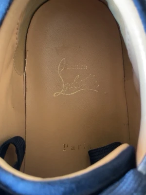 Blå sneakers från Christian Louboutin - Snygga blå sneakers från Christian Louboutin med broderad logga på hälen och ovandel i mocka. Skorna har en klassisk låg siluett och innersula i ljust läder för extra komfort. Perfekta för dig som vill ha något exklusivt och stilrent.