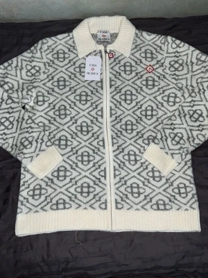 Mönstrad kofta från Casa Blanca - Stilren kofta från Casa Blanca i vitt och grått med grafiskt mönster. Koftan har dragkedja framtill, ribbad krage, muddar och nederkant samt två fickor. Perfekt för dig som gillar en unik och trendig look.