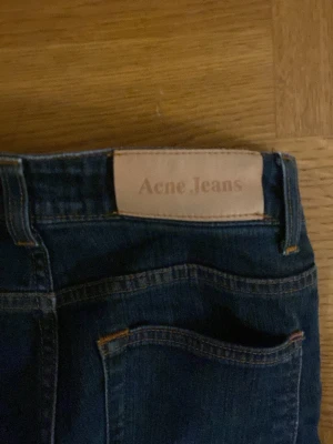 Mörkblå Acne Jeans - Snygga mörkblå jeans från Acne Jeans med klassisk femficksdesign och raka ben. Jeansen har en läderpatch med logotypen på bakfickan och är tillverkade i slitstarkt denim. Perfekta för dig som gillar stilrena och trendiga jeans.