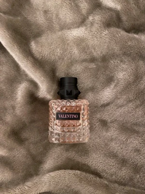 Valentino parfym ( 50ml ) oandvänd! - Säljer en lyxig parfym från Valentino i en genomskinlig glasflaska med nitar och rutmönster. Flaskan har en ljusrosa tonad vätska och ett svart lock med coola detaljer. Perfekt för dig som gillar exklusiva dofter och snygg design. Kartong/ lådan till parfymen förliker med.💕