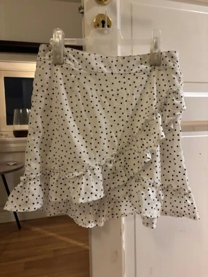 Vit prickig volangkjol med omlott - Supersöt kort kjol i vitt med svarta prickar och volangdetaljer. Kjolen har omlottmodell. Så fin och perfekt nu till sommaren💖
