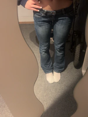 Blå bootcut jeans med låg midja - Säljer ett par klassiska blå bootcut jeans med snygga slitningar och kontrastsömmar. Jeansen har låg midja. Skriv för fler frågor☺️