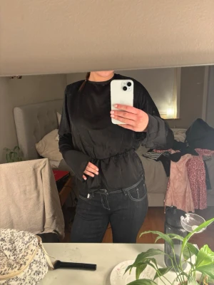 Svart satinblus med öppen rygg - Snygg svart blus i satin med lång ärm och resår i midjan. Blusen har en öppen rygg med knytband upptill. Köpt på bikbok för några år sedan och använt en gång till julfirande, annars aldrig använd. 