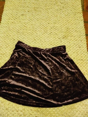 Mörklila sammetskjol Jacqueline de Yong M L - Säljer en mörklila kortkjol i mjuk sammet från Jacqueline de Yong. Kjolen har en enkel, A-linjeformad siluett och bred linning som ger en snygg passform. Perfekt att styla med stickad tröja eller crop top. Den är små I storleken 