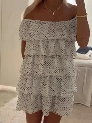 Vit prickig offshoulder volangklänning zara - Supersöt kort vit klänning med svarta prickar och flera volanglager. Offshoulder-modell som ger en trendig vibe, perfekt för varma dagar. Klänningen har en luftig passform och är tillverkad i ett lätt tyg som känns skönt mot huden.