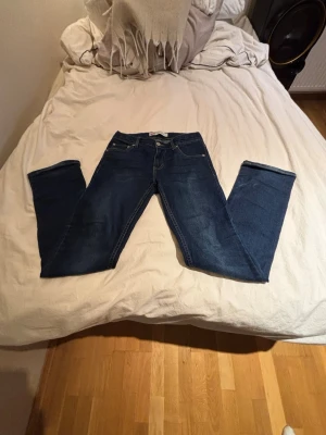 Levi's blå jeans - Säljer ett par klassiska blå Levi's jeans med raka ben och fem fickor. Jeansen har tydliga kontrastsömmar och en brun läderpatch bak i midjan. Tillverkade i slitstark denim, perfekta för en avslappnad och tidlös stil.