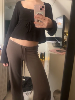 Svart croppad topp med knyt - Säljer en svart croppad topp med långa ärmar och söt knytning i midjan. Toppen har en fyrkantig ringning och är gjord i ett ribbat material som ger en snygg struktur. Perfekt till jeans eller kjol för en trendig look.🩷🩷🩷