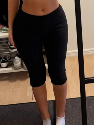 Svarta capri leggings - Säljer ett par svarta capri leggings med ganska låg midja och tight passform. De är stretchiga och bekväma, perfekta för en sportig look eller till vardags. Materialet känns mjukt och följsamt mot kroppen. Inget synligt märke på leggingsen.