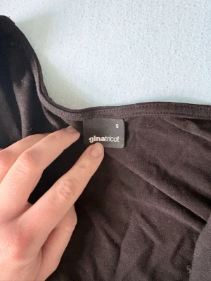 Svart axelbandslös topp Gina Tricot - Säljer en svart topp från Gina Tricot. Toppen har en enkel form med mjukt material, ville bara tillägga att ena av handen är sprättats upp av misstag, men de går att sy den