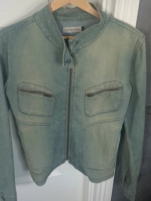 Grön jeansjacka från Terranova - Snygg blå jeansjacka från Terranova med ståkrage och dragkedja framtill. Jackan har två bröstfickor med dragkedja och två stora fickor nedtill. Perfekt för dig som vill ha en unik twist på den klassiska jeansjackan.