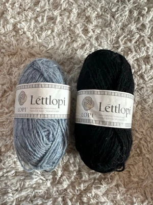 Två nystan Léttlopi ullgarn - Säljer två nystan Léttlopi ullgarn, ett i ljusblått och ett i svart. Perfekt för stickning eller virkning. Varje nystan väger 50g och innehåller 100 meter isländsk ull. Märket är känt för sin höga kvalitet och naturliga känsla.