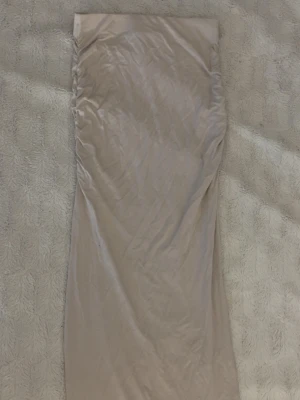 Beige lång kjol med drapering - Snygg beige långkjol med draperade sidor och rak passform. Kjolen har en slät midja och är gjord i ett mjukt, stretchigt tyg som ger en bekväm känsla. Perfekt att styla med en enkel topp eller stickad tröja.