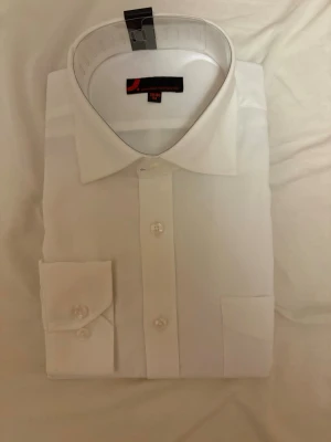 Vit klassisk skjorta från Dressmann - Säljer en vit klassisk skjorta från Dressmann i storlek M (39/40). Skjortan har lång ärm, bröstficka och knappar framtill. Perfekt för en clean och stilren look. Materialet känns mjukt och bekvämt, och kragen är klassiskt skuren.