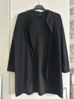 Svart öppen cardigan från Sisterspoint - Stilren svart cardiganjacka från Sisterspoint med öppen front och trekvartsärmar. Lätt och mjukt material som faller snyggt. Perfekt att slänga över en t-shirt eller topp för en enkel och clean look.