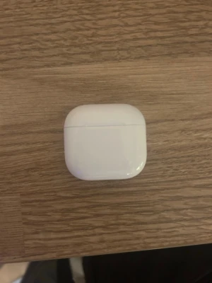 AirPods 4 - Säljer ett par vita trådlösa hörlurar från Apple med laddningsetui. Etuiet är kompakt, har rundade kanter och är gjort i blank plast. Perfekt för dig som vill ha smidiga hörlurar till mobilen eller datorn.