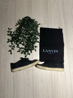 Svarta Lanvin sneakers i läder - Snygga svarta sneakers från Lanvin med ovandel i strukturerat läder och klassisk vit sula. Skorna har svarta skosnören och en stilren, låg profil som passar till det mesta. Kommer med originalpåse från Lanvin. Det är inte riktigt den vanliga modellen men riktigt snygga ändå!😀