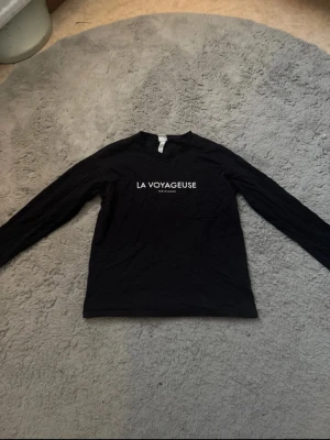 Svart långärmad tröja H&M - Svart långärmad tröja från H&M med trycket 'LA VOYAGEUSE' i vitt framtill. Kommer inte till användning längre.
