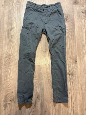  Nudie Jeans - Snygga grå chinos från Nudie Jeans med raka ben och klassisk passform. Byxorna har sidofickor och bälteshällor, tillverkade i mjuk bomull för en bekväm känsla. Perfekta för dig som gillar stilrena och avslappnade plagg.