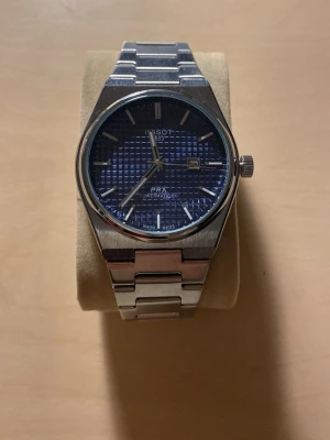 Tissot PRX Powermatic 80 blå urtavla - Snygg Tissot PRX Powermatic 80 med blå urtavla och datumvisning. Klockan har ett stilrent armband i rostfritt stål och en klassisk rund boett. Perfekt accessoar för dig som gillar tidlös design och kvalitetskänsla.