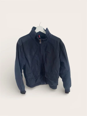 Tommy Hilfiger Jacka / Bomber – Marinblå (Strl XL) - Säljer en klassisk och mångsidig jacka från Tommy Hilfiger. Modellen är en variant av "Harrington/Bomber" med hög krage och muddar i ärmslut och midja som håller passformen snygg.   Två rejäla fickor fram med knappstängning. Perfekt vår- och höstjacka som funkar lika bra till jeans som till chinos.  Skick: Bra begagnat skick. Hel och fullt fungerande dragkedja.  Storlek: XL (Extra Large). Pris: 500 kr Nypris ca 2 500 kr.