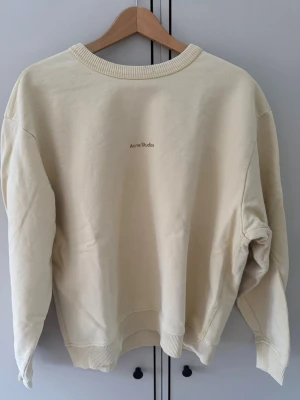 Acne Studios Sweatshirt  - Säljer en stilren gul sweatshirt från Acne Studios. Tröjan har rund halsringning, ribbade muddar vid ärmslut och nederkant samt diskret logga på bröstet. Tillverkad i mjuk bomullsblandning och har en relaxed fit som passar perfekt till jeans eller sweatpants. Två små fläckar som visas på bilderna