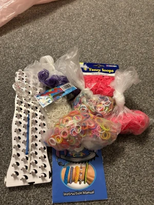 Set för att göra armband med gummiband - Säljer ett komplett set för att göra egna armband med färgglada gummiband. Innehåller massor av elastiska band i olika färger, en vit plastplatta för att fläta, krok och instruktioner. Perfekt för dig som vill skapa personliga smycken med pärl-liknande känsla.