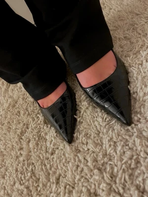 Svarta pumps med krokodilmönster - Snygga svarta pumps från ASOS med spetsig tå och blockklack. Skorna har ett glansigt krokodilmönstrat material som ger en trendig look. Perfekta för dig som vill sticka ut med stilrena detaljer och modern design. ❣️