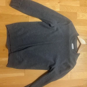 Grå merinoulltröja These Glory Days - Mörkgrå stickad tröja från These Glory Days i mjuk superior merinoull. Klassisk rak modell med rund halsringning och ribbade muddar vid ärmslut och nederkant. Perfekt för lager på lager och enkel att matcha.