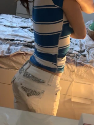 Vita jeans med blingade fickor - Säljer ett par vita jeans med raka ben och låg midja. Baksidan har snygga detaljer med bling och broderier på fickorna som ger en extra touch. Perfekta för dig som vill sticka ut lite extra med din outfit.