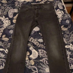 Svarta raka jeans från nudie  - Säljer ett par svarta jeans med rak passform och klassisk femficksdesign. Jeansen har en diskret tvättad look och är tillverkade i denim. Perfekta för en avslappnad och stilren outfit.